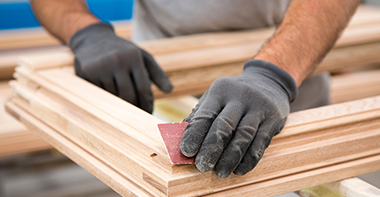 a joiner wearing black gloves using sandpaper to sand a frame for a window in a workshop